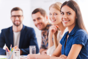 Group of confident business people in smart casual wear sitting at the table together and smiling